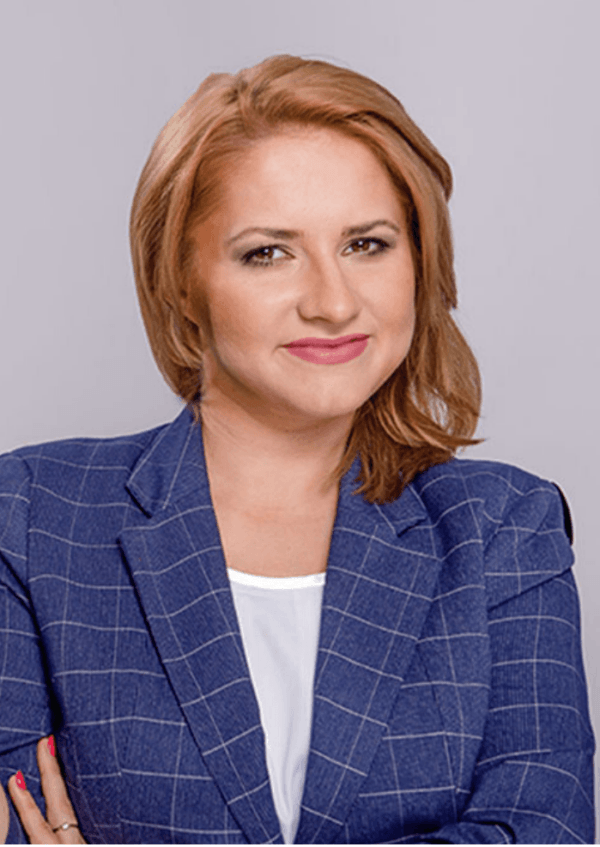 Uśmiechnięta Katarzyna Bieleniewicz, certyfikowany trener instytutu Gallupa z rozpuszczonymi włosami w marynarce w kratkę.